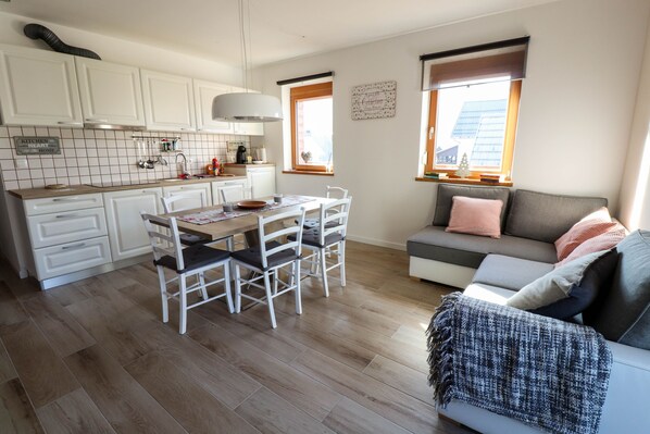 A compact kitchen with white cabinets, a dining table with chairs, and a sofa with a blanket.