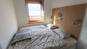 A small, neatly made bed with patterned bedding, a bedside lamp, and a window with a view of buildings outside. - Old Village House - Holiday Nest (Bohinjska Bistrica)