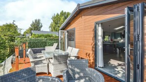 Une terrasse extérieure moderne, dotée de meubles en osier et d’une porte vitrée donnant sur la cuisine.