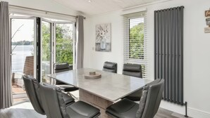 Un espace de salle à manger moderne, doté d’une grande table, de six chaises et offrant une vue sur un lac grâce à de larges fenêtres.