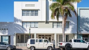 A two-story building with a white facade, a palm tree in front, and a white van parked in front. - Miami Beach 1BR · 2 Blocks to Sand on Collins Ave (Miami Beach)