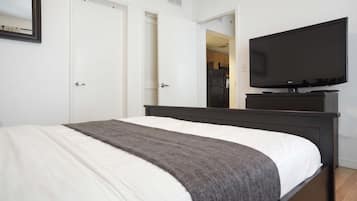 A bedroom with a bed, a television on a stand, and a door leading to a kitchen.