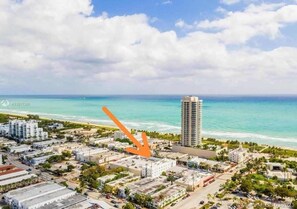 An aerial view of a coastal city with a prominent high-rise building, a beach, and a mix of residential and commercial buildings. - Miami Beach 1BR · 2 Blocks to Sand on Collins Ave (Miami Beach)