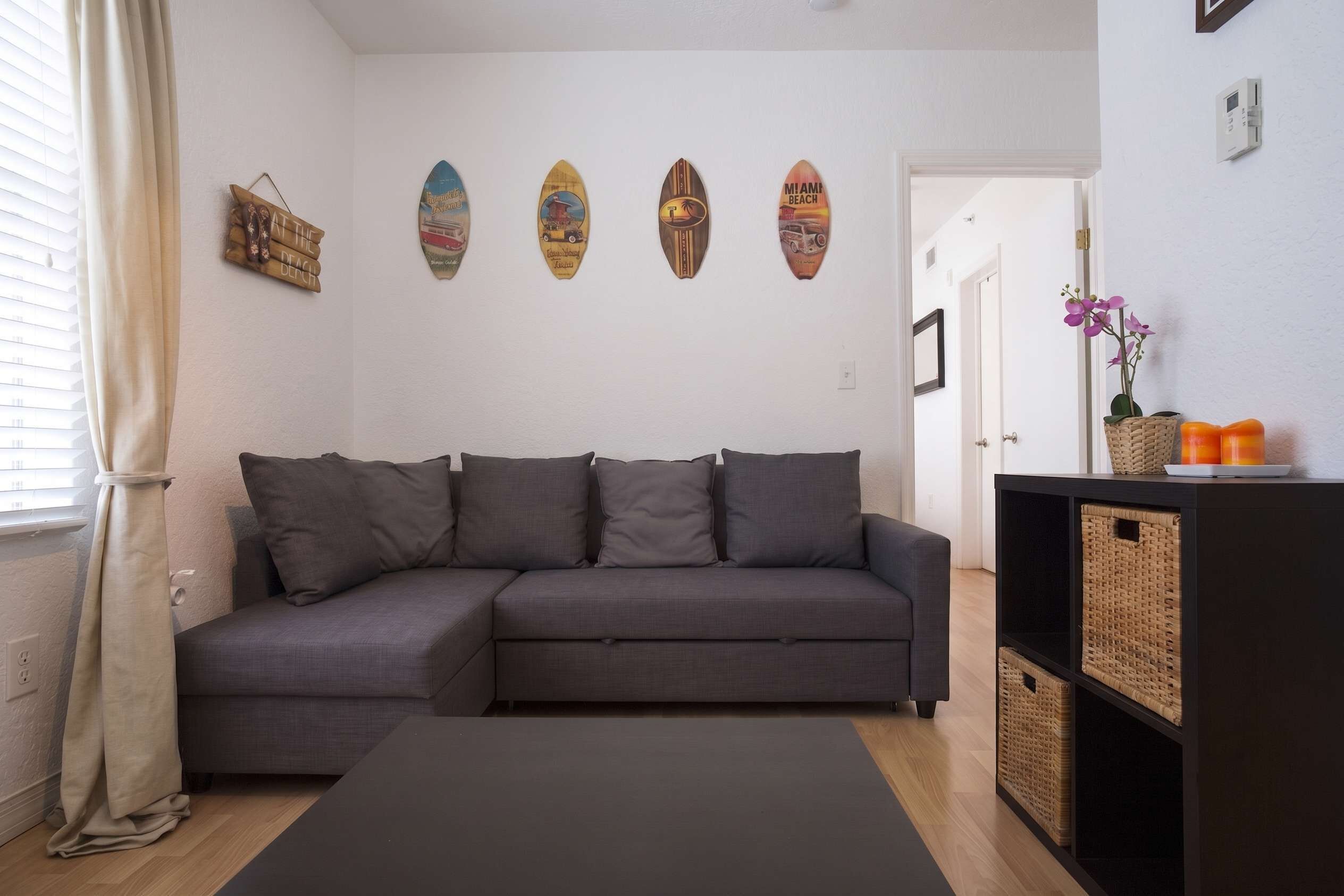 A modern living room with a grey sectional sofa, a black ottoman, and a wall decorated with surfboards.