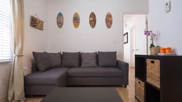 A modern living room with a grey sectional sofa, a black ottoman, and a wall decorated with surfboards.