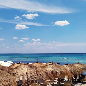 A beach with thatched umbrellas and lounge chairs, a clear blue sky, and the ocean in the background. - MarGi House, 1968 (Lecce)