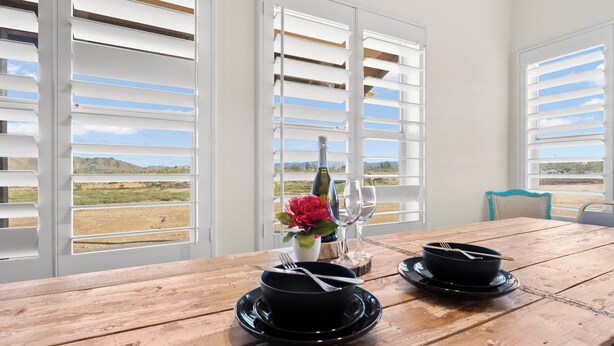 A dining table with black bowls and a bottle, set against a backdrop of a scenic view through large windows with white shutters. - Dark Horse Ranch · Single-Story Home on 5 Acres · Sleeps 8 · Dog-Friendly (Yucca Valley)