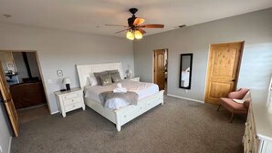 A bedroom with a white bed, a nightstand, a dresser, a ceiling fan, and a door. - Dark Horse Ranch · Single-Story Home on 5 Acres · Sleeps 8 · Dog-Friendly (Yucca Valley)