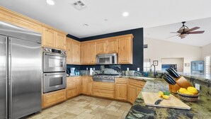 A modern kitchen with stainless steel appliances, wooden cabinets, granite countertops, and a ceiling fan. - Dark Horse Ranch · Single-Story Home on 5 Acres · Sleeps 8 · Dog-Friendly (Yucca Valley)