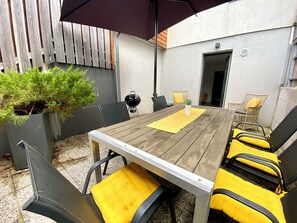 A wooden table with yellow cushions, surrounded by chairs, under a large umbrella.
