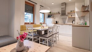 A modern kitchen with white cabinets, a dining area with a wooden table and chairs, and a view of the outside through a window. - Old Village House - Catherine's place (Bohinjska Bistrica)