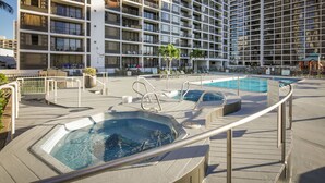 Zona de piscina en la azotea con jacuzzis y sillas de descanso, rodeada por un edificio de gran altura con balcones.