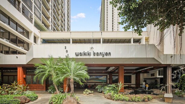 Un edificio moderno con un letrero que dice "wakiki banyan". Tiene una entrada cubierta, senderos de piedra y diversas plantas.