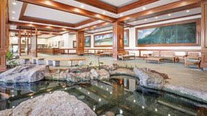 Eine geräumige Lobby mit einem zentralen Wasserspiel, hölzernen Bänken und großen Fenstern mit Blick auf die Berge.