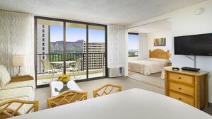 Ein Hotelzimmer mit Balkon, einem Bett, einem Fernseher und einem Schreibtisch mit Stuhl.