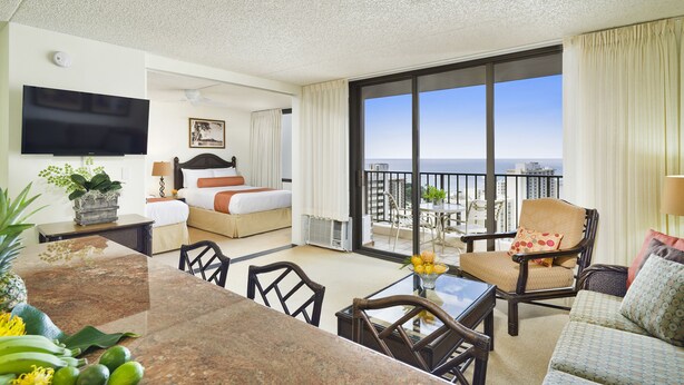 A hotel room with a balcony, a bed, a TV, a dining area, and a view of the ocean. - Sweeping Ocean Views | Aston Waikiki Banyan 1BOV3 – Pool & Hot Tub (Honolulu)