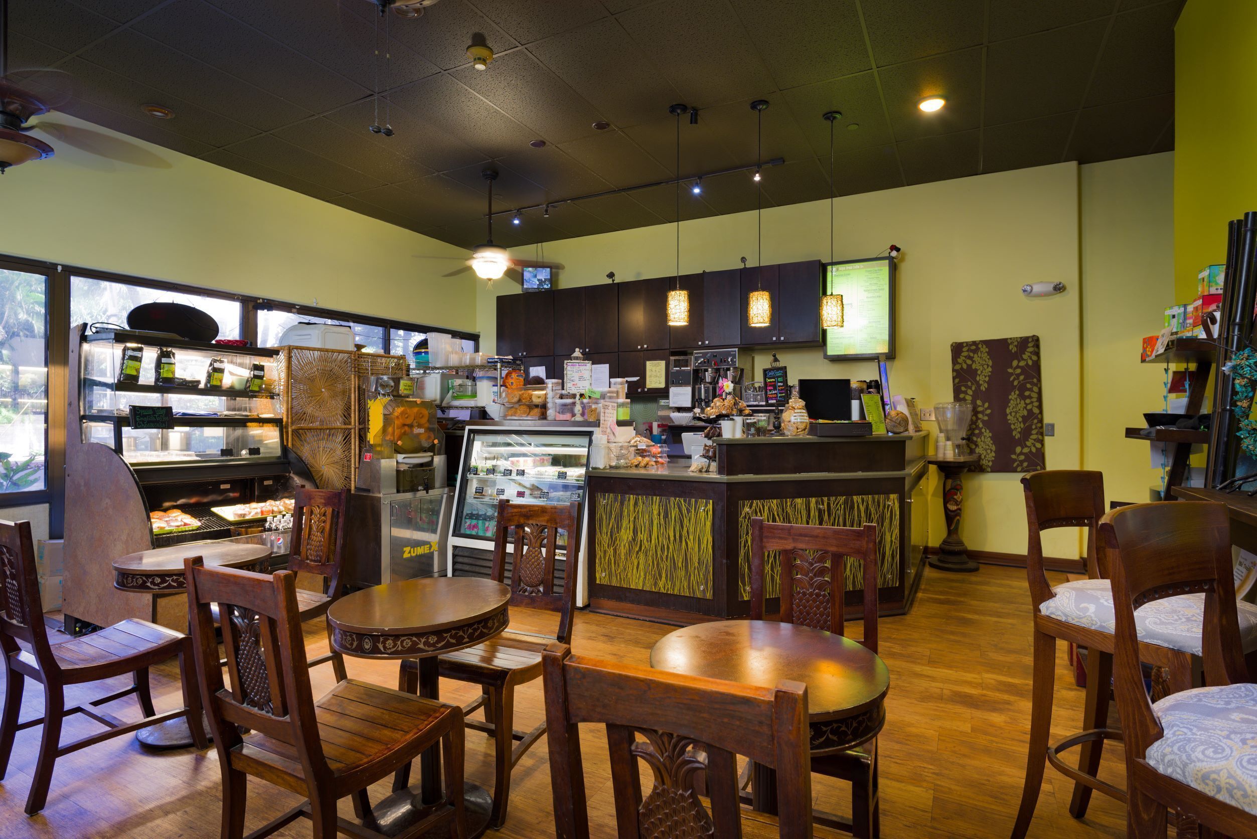 A restaurant interior with wooden tables and chairs, a counter with a cash register, and a refrigerated display case.