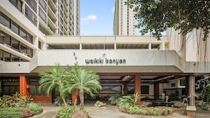Un edificio moderno con un letrero que dice "wakiki banyan". Tiene una entrada cubierta, senderos de piedra y diversas plantas.