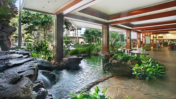 Vestíbulo de hotel con fuente de agua, plantas de interior y suelo de piedra.