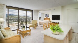 Habitación de hotel con balcón, cama, escritorio, televisor y vista panorámica de la ciudad.