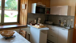 Une cuisine compacte aux murs en bois, équipée d’un four à micro-ondes, d’un évier et d’une fenêtre donnant sur un paysage verdoyant.