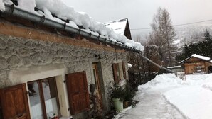 Un bâtiment en pierre avec des volets en bois et un toit recouvert de neige.