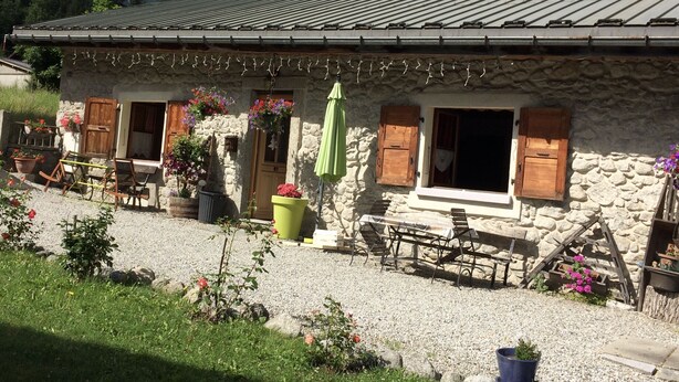 Un bâtiment en pierre avec un toit en pente, des volets en bois et une allée gravillonnée.