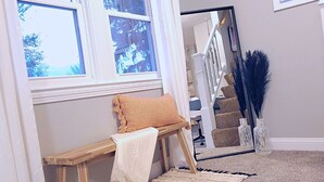 Een kamer met een bank, een witte vloerkleed, een trap en een spiegel die de trap weerkaatst.
