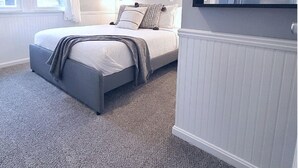 Een slaapkamer met een bed, een plafondventilator, een raam met gordijnen, een ingelijst schilderij aan de muur en een bordje op de deur.
