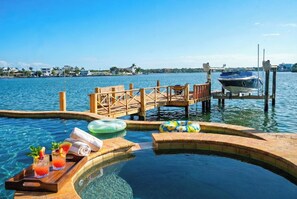 Un espace piscine doté d’une terrasse en bois, de chaises longues et d’un bateau amarré au fond.