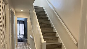 A wooden staircase with white railings leading to a room with a door and a window with curtains. - Spacious, cozy villa in Coligny Villas (Hilton Head Island)
