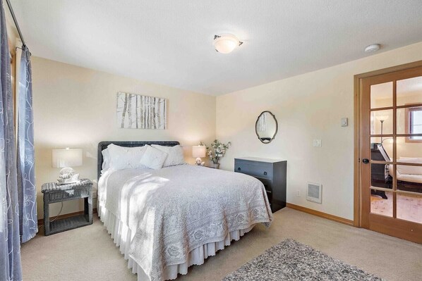 Une chambre à coucher comprenant un lit, des tables de chevet, une commode, un miroir et une porte donnant sur une vue agréable.
