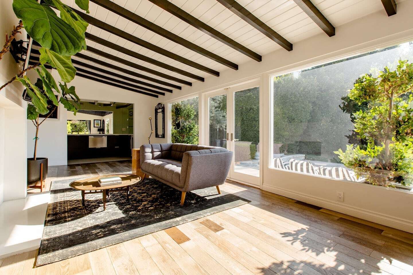 A modern living room with a sofa, coffee table, and large windows overlooking a garden.