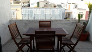 A small outdoor patio with a wooden table and chairs, a potted plant, and a view of the cityscape.