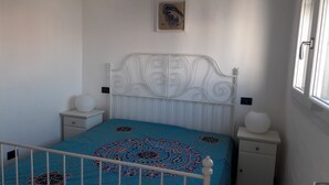 A bedroom with a white metal headboard, a blue patterned bedspread, two bedside tables with white lamps, and a single framed artwork on the wall.