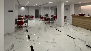 A modern hotel lobby with marble flooring, red and grey chairs, and a wooden reception desk. - Relax Mea Hotel (Sarandë)