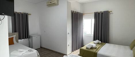 Una habitación de hotel con dos camas, televisión, aire acondicionado y ventana con cortinas.