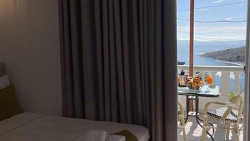 A hotel room with a bed, a table with fruit and drinks, and a view of the sea.