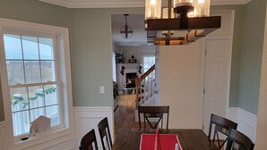 Un coin repas avec une table en bois, des chaises et un chemin de table rouge. Un lustre est suspendu au-dessus de la table.