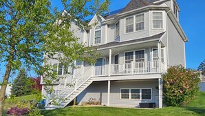 Une maison à deux étages avec un porche à l’avant, un escalier menant au deuxième étage et une pelouse bien entretenue.