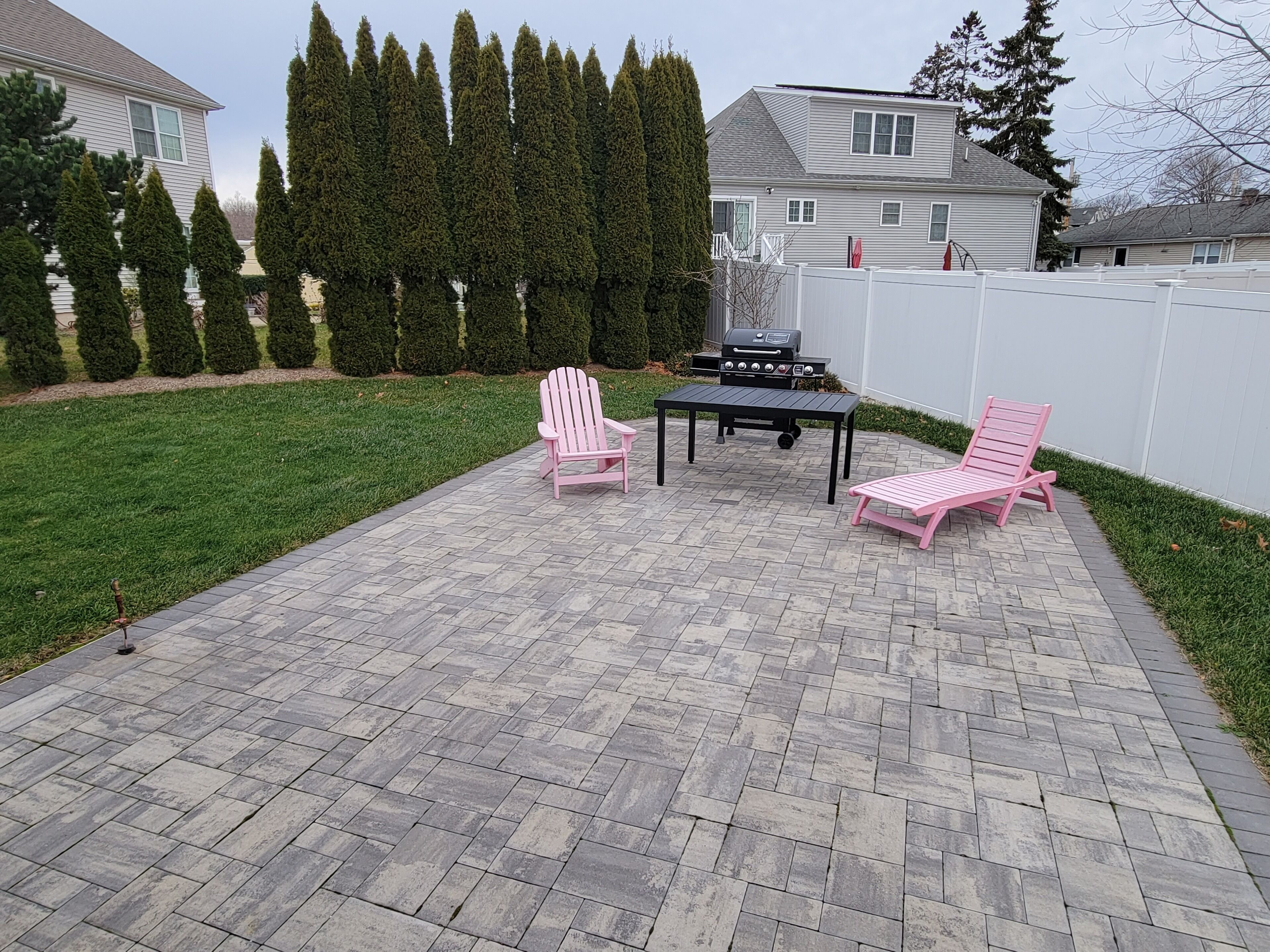 A patio area with a grill, two Adirondack chairs, and a table.