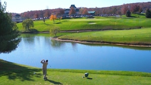 Un campo de golf con un estanque, una persona jugando al golf y un edificio al fondo.