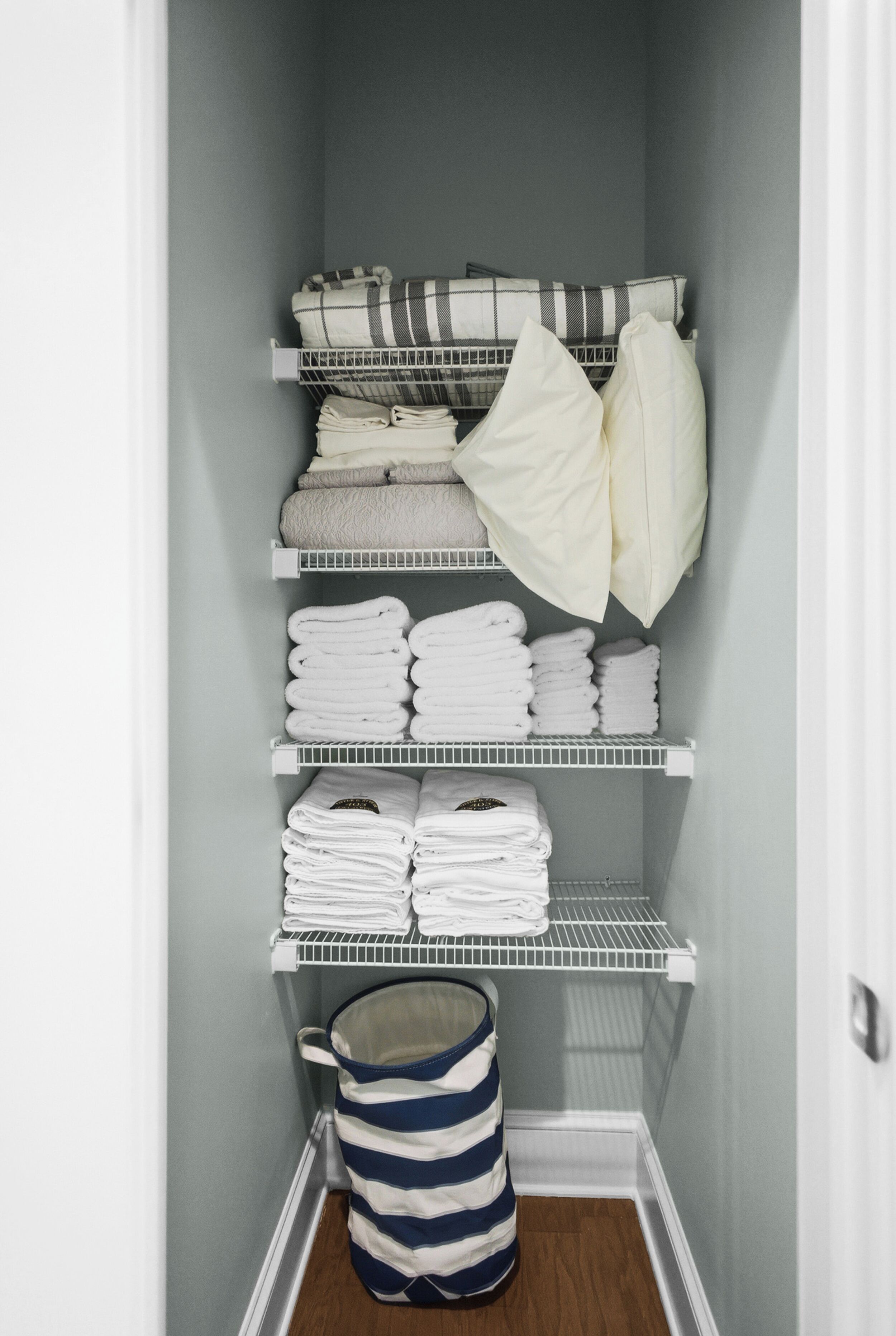 A storage closet with shelves holding folded towels and a striped bag.
