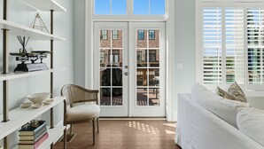 A room with a white sofa, a wicker chair, a bookshelf, and a double door leading to an outdoor patio. - Watch Cargo Ships Glide by from This Walkable Savannah River Retreat (Savannah)