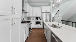 A modern kitchen with white cabinetry, stainless steel appliances, and a wooden floor. - Watch Cargo Ships Glide by from This Walkable Savannah River Retreat (Savannah)
