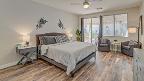 Quarto com cama, mesas de cabeceira, ventilador de teto, janela com cortinas e vista para o exterior.