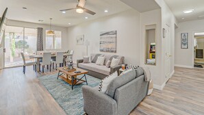 Uma sala de estar espaçosa com um sofá cinzento, uma mesa de centro e um espaço de jantar com mesa e cadeiras.
