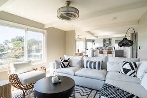 Una sala moderna con un sofá, sillones y una mesa de centro. Una ventana grande ofrece vistas al exterior.