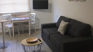A living room with a black sofa, a TV mounted on the wall, a dining table with chairs, and a small round table with a bowl and a remote control. - MAXORATA TOWN FUERTEVENTURA (Morro Jable)
