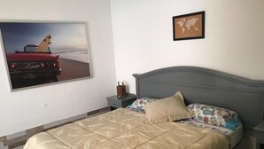A bedroom with a bed, a nightstand, a framed world map, and a picture of a car on the wall. - MAXORATA TOWN FUERTEVENTURA (Morro Jable)